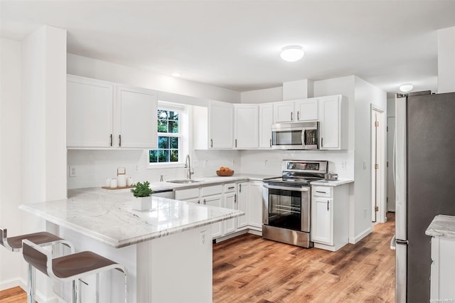 kitchen featuring kitchen peninsula, appliances with stainless steel finishes, light wood-type flooring, sink, and white cabinets