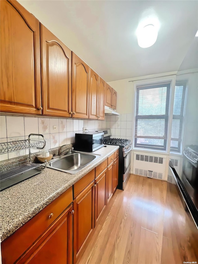 kitchen with appliances with stainless steel finishes, light wood-type flooring, tasteful backsplash, sink, and radiator heating unit