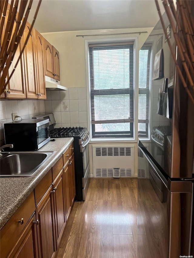 kitchen with radiator, sink, dark hardwood / wood-style flooring, backsplash, and appliances with stainless steel finishes