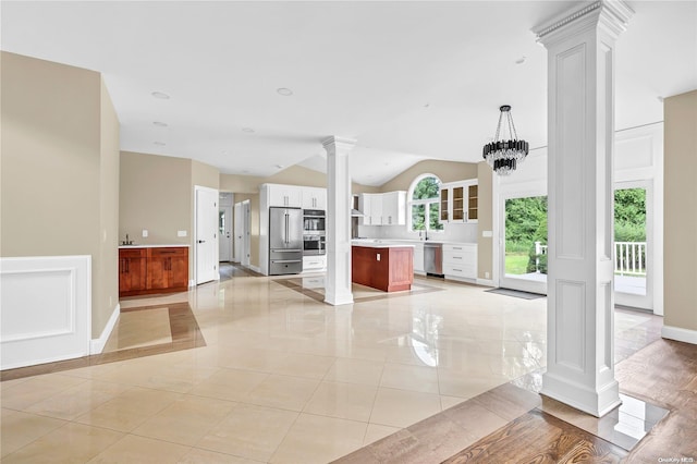 unfurnished living room featuring decorative columns, lofted ceiling, and an inviting chandelier