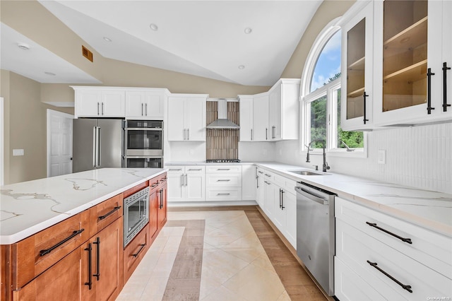 kitchen with wall chimney exhaust hood, white cabinetry, lofted ceiling, and stainless steel appliances