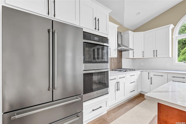 kitchen with light stone countertops, wall chimney exhaust hood, stainless steel appliances, white cabinets, and lofted ceiling