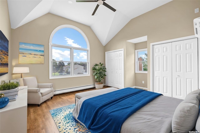 bedroom with light wood-type flooring, vaulted ceiling, ceiling fan, a baseboard heating unit, and multiple closets