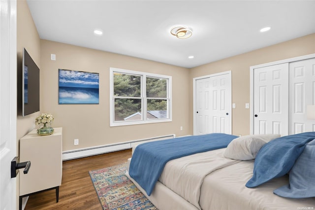 bedroom with baseboard heating, dark hardwood / wood-style flooring, and two closets