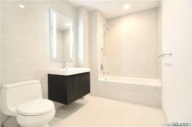 full bathroom with tiled shower / bath combo, tile patterned flooring, toilet, vanity, and tile walls