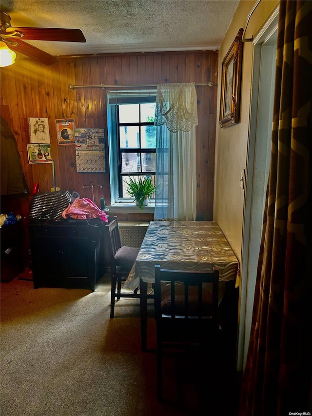 carpeted dining space featuring ceiling fan, a textured ceiling, and wooden walls