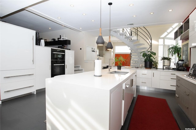 kitchen with white cabinets, hanging light fixtures, sink, and a kitchen island with sink