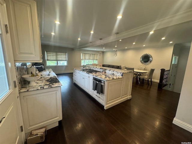 kitchen with hanging light fixtures, light stone countertops, ornamental molding, a kitchen island, and dark hardwood / wood-style flooring