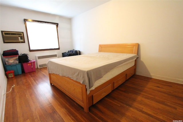 bedroom with dark hardwood / wood-style flooring, a wall unit AC, and radiator