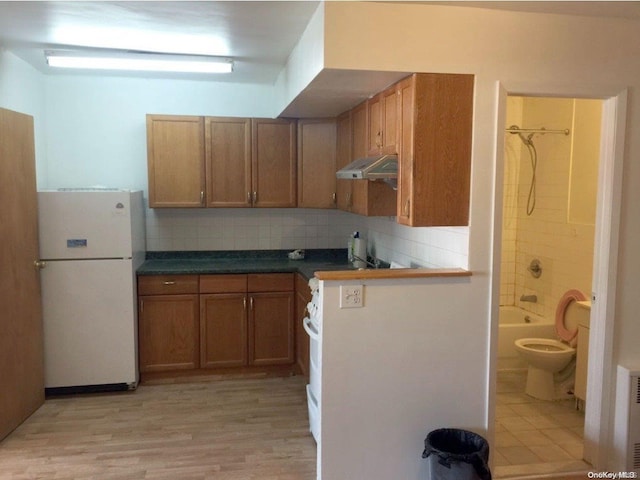 kitchen featuring backsplash, light hardwood / wood-style floors, exhaust hood, radiator heating unit, and white fridge