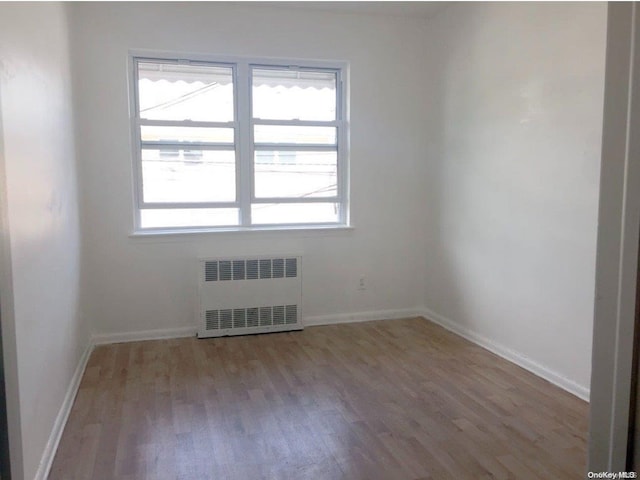 empty room with a wealth of natural light, radiator heating unit, and light hardwood / wood-style floors