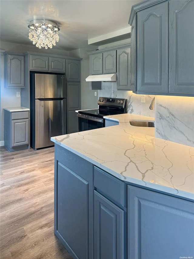 kitchen with light stone countertops, light wood-type flooring, tasteful backsplash, stainless steel appliances, and a chandelier