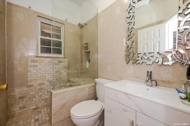 bathroom with vanity, decorative backsplash, toilet, tile walls, and a tile shower