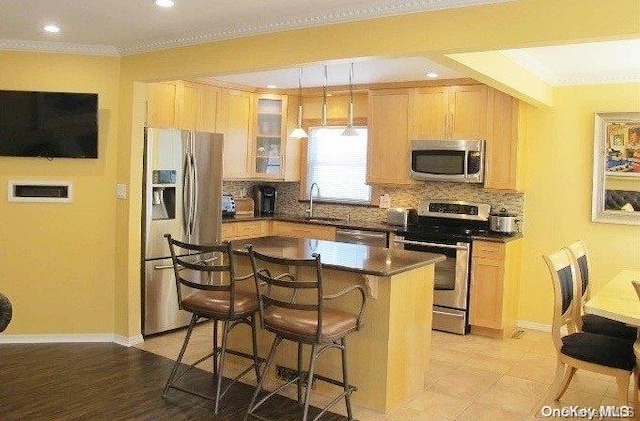 kitchen featuring backsplash, appliances with stainless steel finishes, decorative light fixtures, a kitchen island, and a breakfast bar area