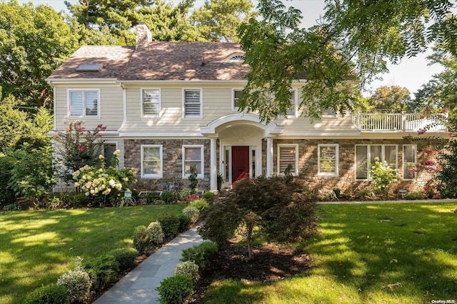 colonial-style house featuring a balcony and a front lawn