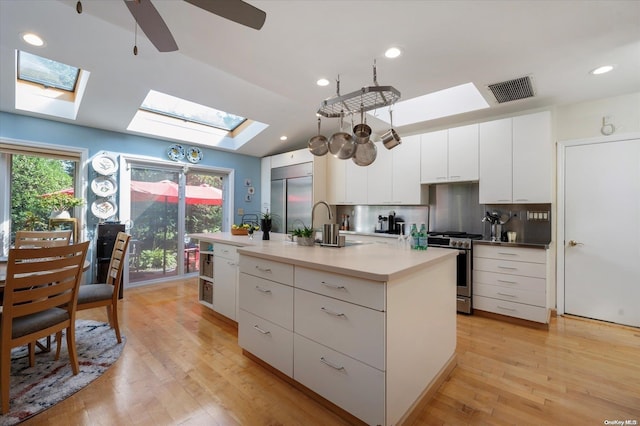 kitchen with white cabinetry, an island with sink, stainless steel appliances, and lofted ceiling