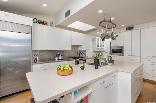 kitchen with built in appliances, white cabinetry, a kitchen island with sink, and light hardwood / wood-style flooring