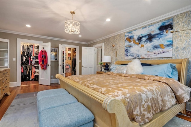 bedroom featuring crown molding, a chandelier, a walk in closet, a closet, and hardwood / wood-style flooring