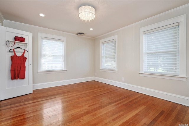 empty room featuring crown molding, plenty of natural light, an inviting chandelier, and hardwood / wood-style flooring