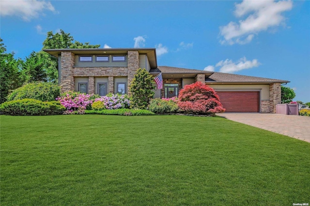 prairie-style home featuring stone siding, an attached garage, driveway, and a front lawn