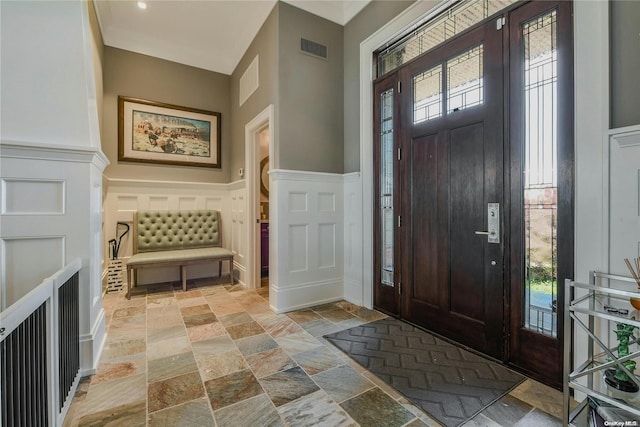 entryway featuring wainscoting, visible vents, a decorative wall, and stone tile floors