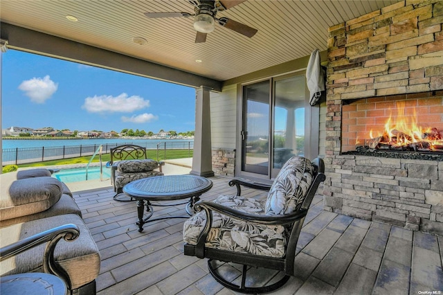 view of patio / terrace featuring a ceiling fan, a fenced in pool, a water view, fence, and an outdoor stone fireplace