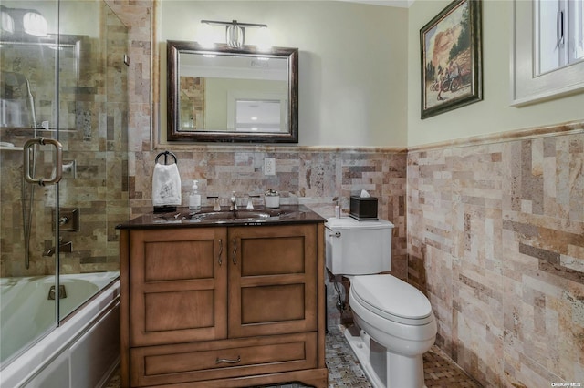 full bath featuring tile walls, toilet, wainscoting, combined bath / shower with glass door, and vanity