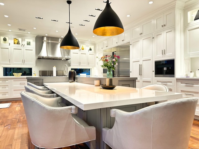 kitchen featuring decorative light fixtures, a spacious island, glass insert cabinets, and range hood