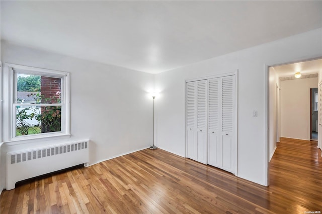 unfurnished bedroom featuring hardwood / wood-style floors, radiator, and a closet