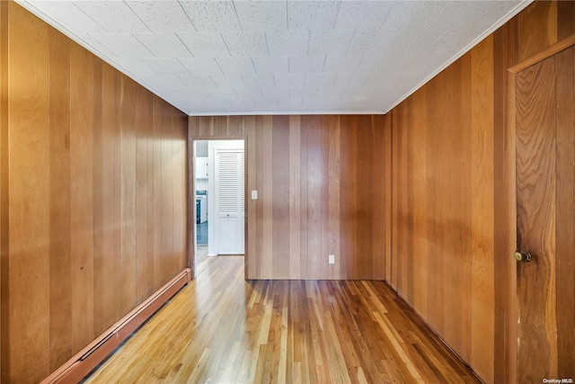 unfurnished room with light hardwood / wood-style floors, a baseboard radiator, and wood walls