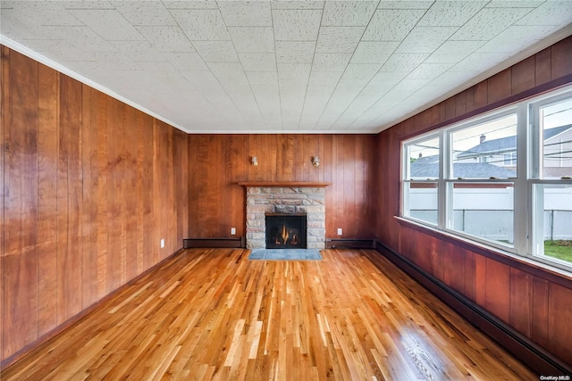 unfurnished living room with wood walls, a healthy amount of sunlight, a stone fireplace, and light wood-type flooring