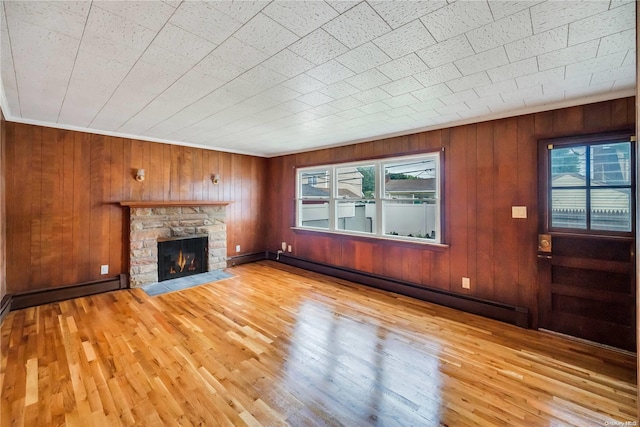 unfurnished living room with wood walls, a stone fireplace, a baseboard heating unit, and light hardwood / wood-style flooring