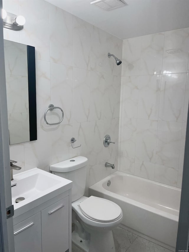 full bathroom featuring tiled shower / bath, vanity, toilet, and tile walls