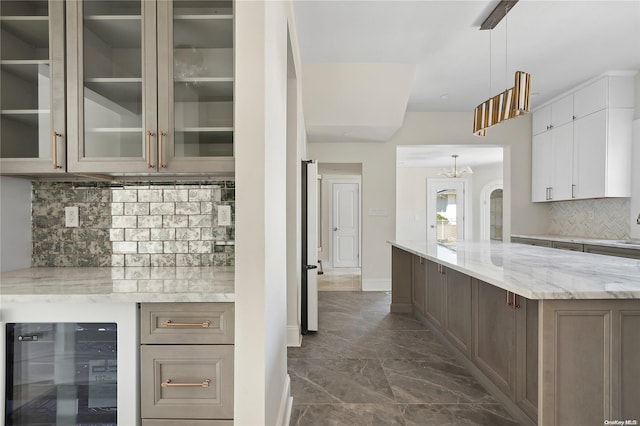 kitchen with decorative backsplash, wine cooler, light stone counters, white cabinetry, and hanging light fixtures