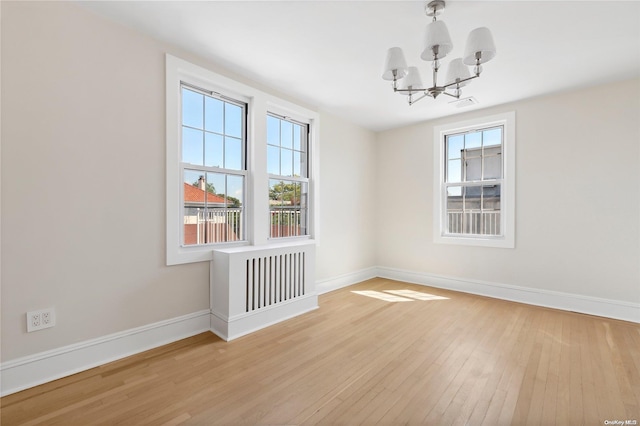 empty room with a notable chandelier and light hardwood / wood-style flooring