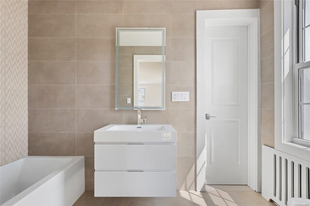 65 W Beech St, Long Beach, NY 11561 - bathroom with tile walls, vanity, tile patterned flooring, radiator heating unit, and a tub to relax in