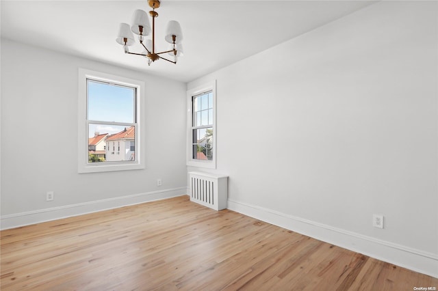 spare room with a notable chandelier, light wood-type flooring, and radiator