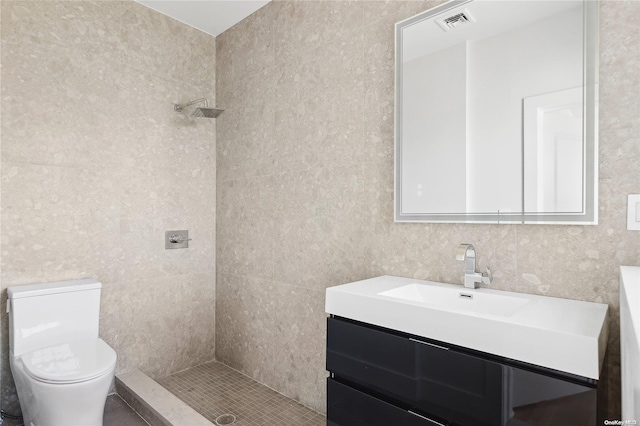 bathroom featuring vanity, toilet, tile walls, and a tile shower