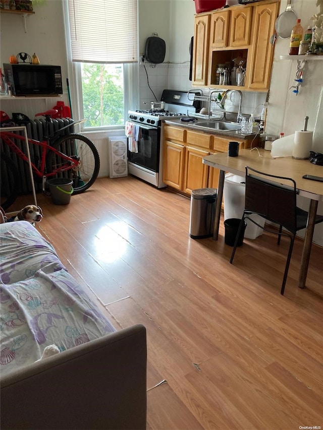 kitchen with gas stove, backsplash, sink, and light wood-type flooring