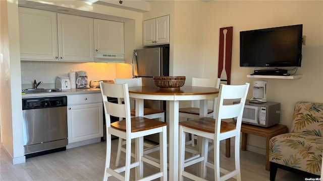 kitchen featuring sink, light hardwood / wood-style flooring, decorative backsplash, white cabinets, and appliances with stainless steel finishes