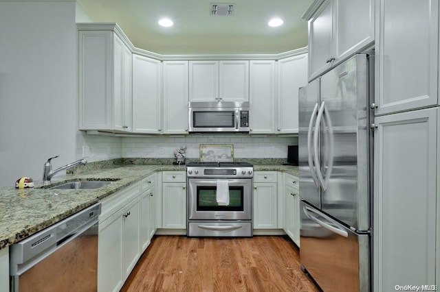 kitchen with sink, light wood-type flooring, appliances with stainless steel finishes, light stone counters, and white cabinetry