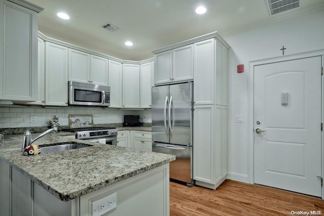 kitchen with appliances with stainless steel finishes, backsplash, light stone counters, sink, and light hardwood / wood-style flooring