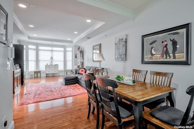 dining area with light wood-type flooring, a tray ceiling, and crown molding