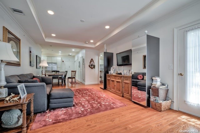 living room with light wood-type flooring, a tray ceiling, and crown molding