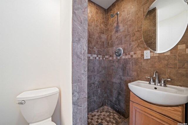 bathroom with a tile shower, vanity, toilet, and backsplash