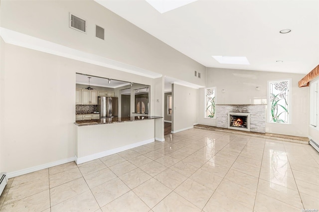 unfurnished living room featuring a fireplace, light tile patterned floors, baseboard heating, and vaulted ceiling with skylight