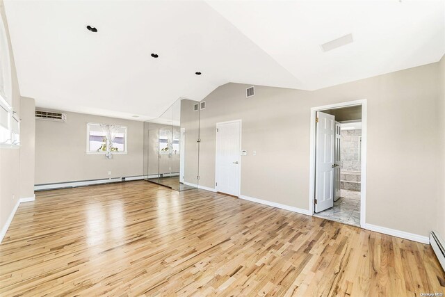 unfurnished room with light hardwood / wood-style floors, a wall mounted AC, a baseboard radiator, and vaulted ceiling