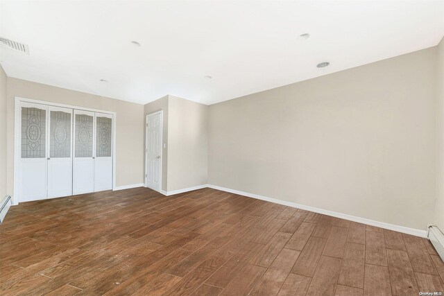 unfurnished bedroom featuring dark wood-type flooring and a baseboard heating unit