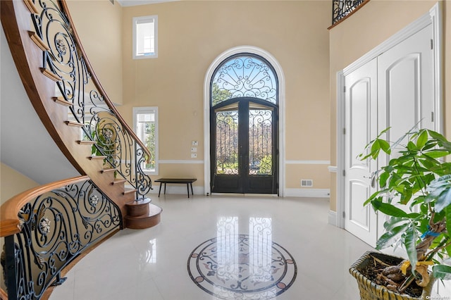 tiled entryway featuring french doors, a towering ceiling, and a healthy amount of sunlight