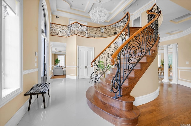 staircase with ornamental molding, decorative columns, an inviting chandelier, and a healthy amount of sunlight